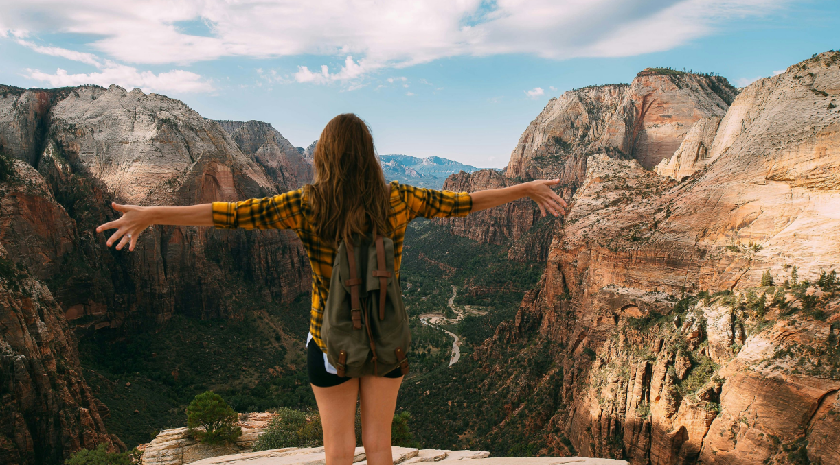 A woman standing on a cliff edge with her arms outstretched, embracing the fresh mountain air and stunning canyon view, symbolizing the confidence and freshness provided by using deodorant.