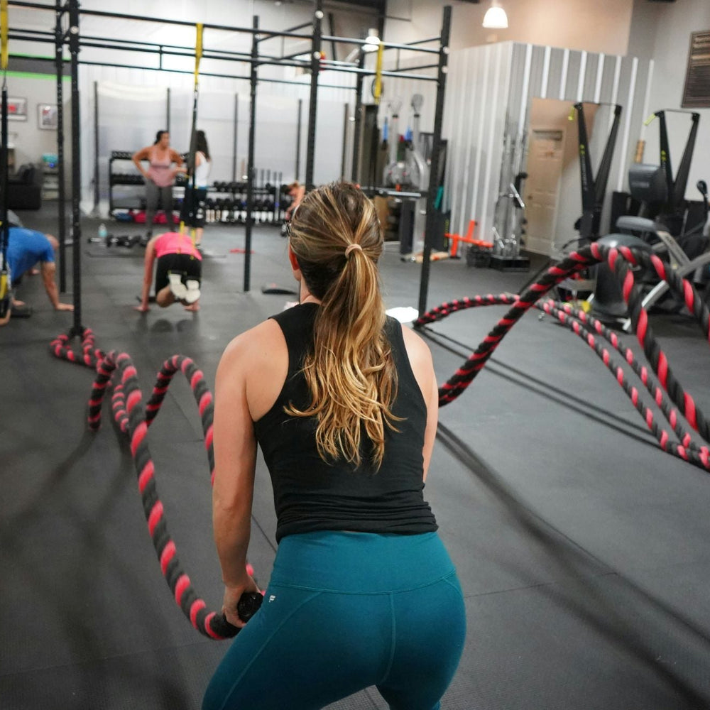 Woman working out with battle ropes in a gym, staying fresh and odor-free with stick deodorant.